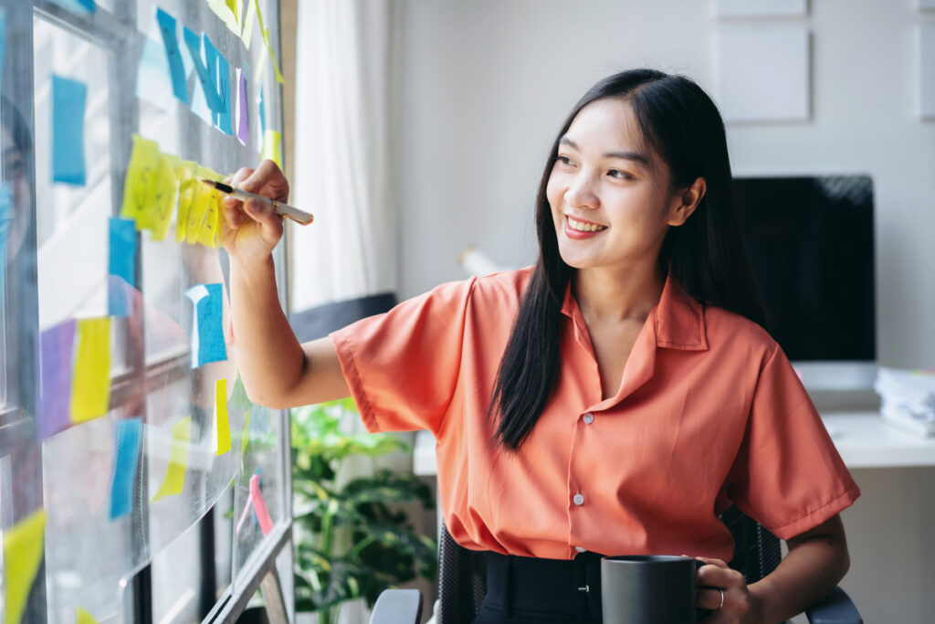 A young professional writing on sticky notes posted on a glass board.