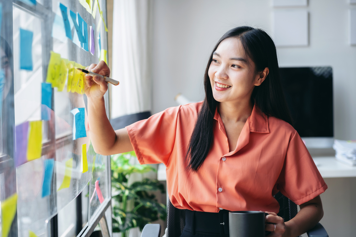 A young professional writing on sticky notes posted on a glass board.